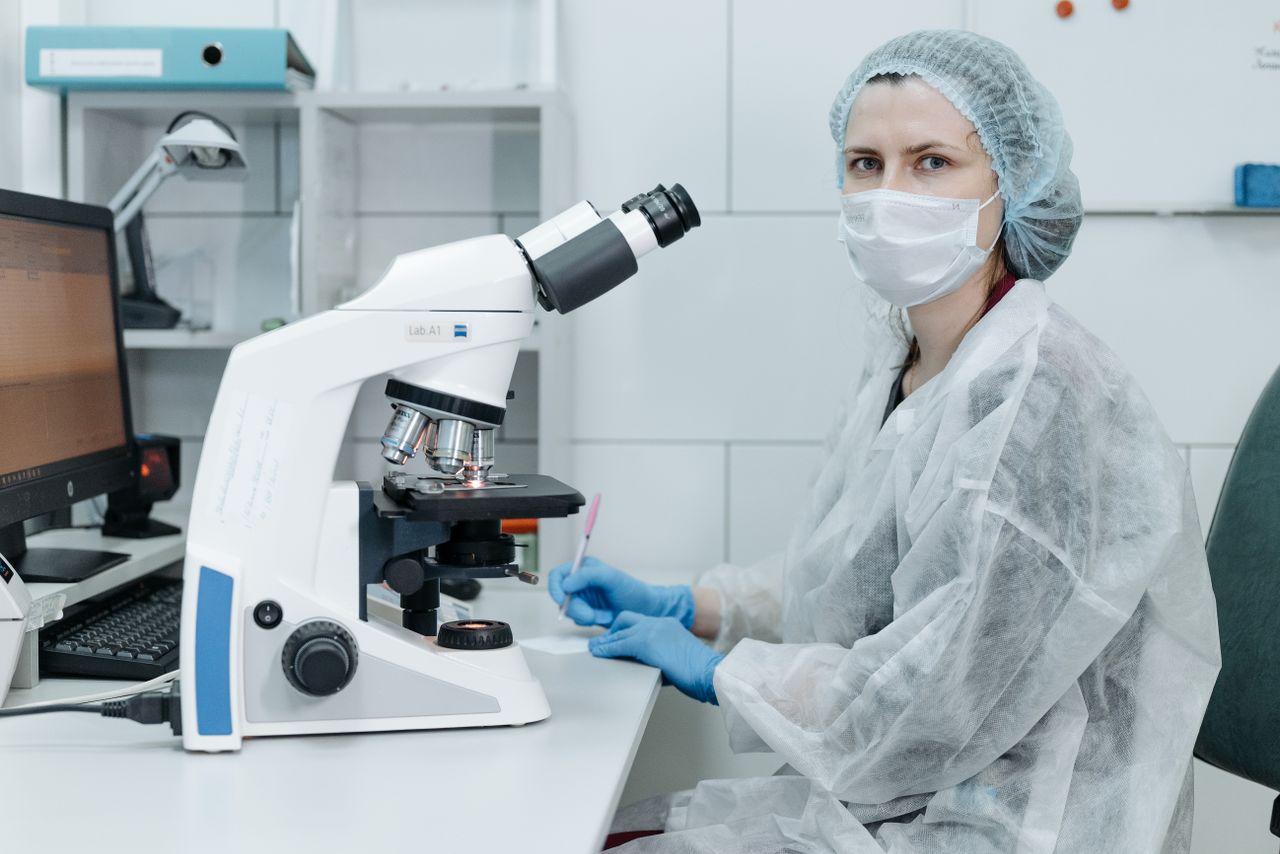 Scientist in protective gear using a microscope in a modern lab setting.