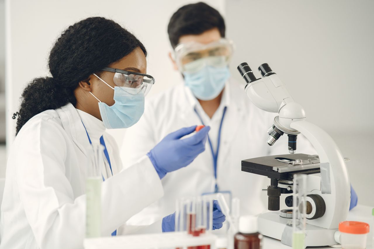 Researchers in protective gear conduct scientific experiments using microscopes in a lab.