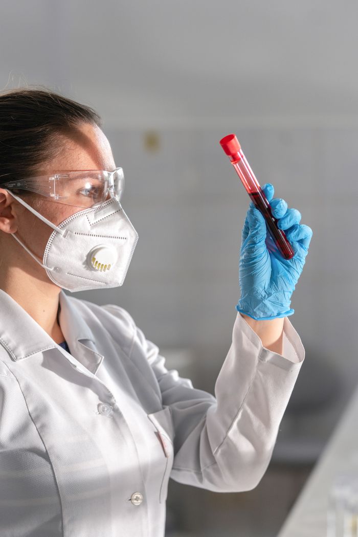 A female scientist in protective gear examines a blood sample in a laboratory setting.